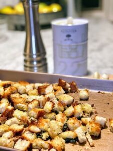 homemade croutons on a baking sheet with a can of French Olive Oil and garlic cloves
