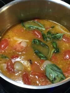 A pot of simmering tomato soup with fresh basil